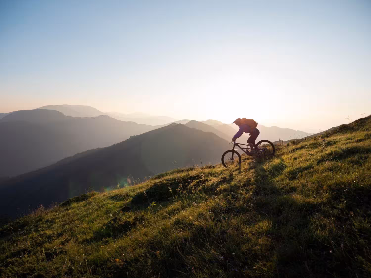 Foto eines Fahrradfahrers, der einen Berg bei Sonnenaufgang hinunter fährt
