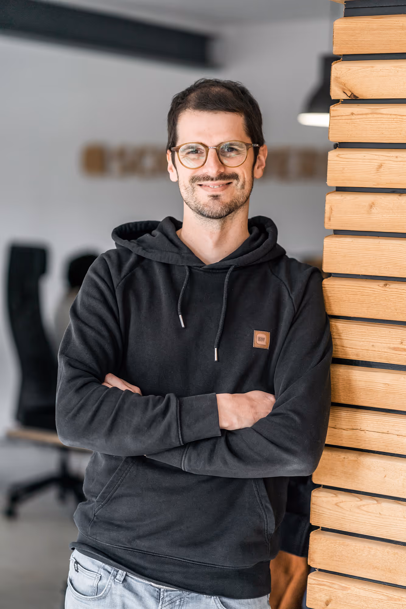 Tobi, Geschäftsführer von Schaltwerk Digital, steht mit verschränkten Armen lächelnd im Büro.